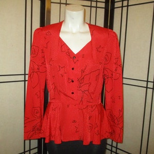 Könnte beinhalten: Eine rote Bluse mit einem schwarzen abstrakten Blumendruck und Knopfleiste vorne. Die Bluse hat einen Peplum-Saum und lange Ärmel.