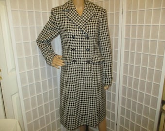May include: A black and cream houndstooth double-breasted coat. The coat has a notched collar, two rows of black buttons, and a knee-length hem. The classic pattern and tailored design create a sophisticated look.