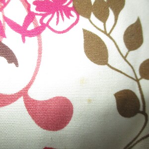 May include: Close-up of a white fabric with a floral pattern. The design features pink and brown stylized flowers and leaves. The fabric has a textured appearance.