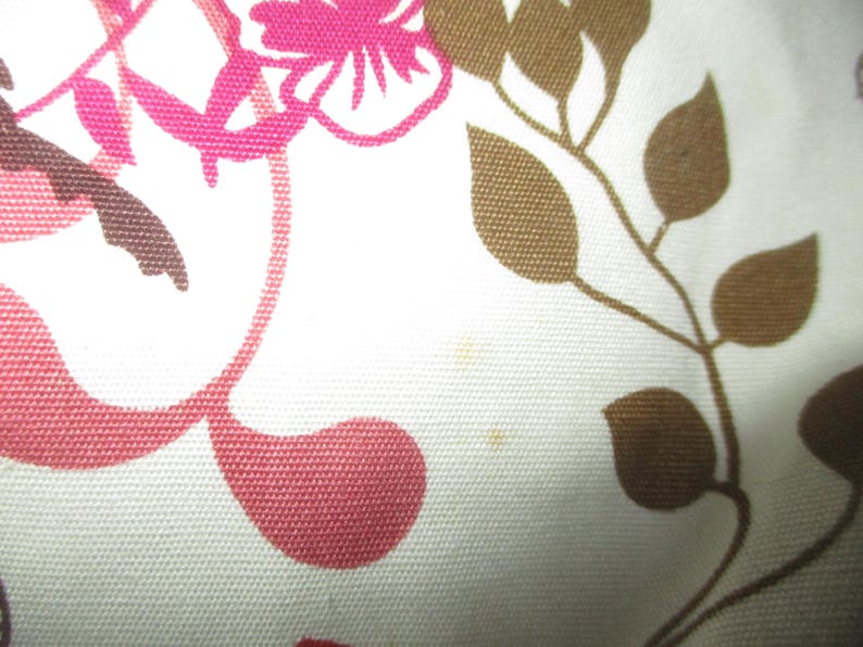 May include: Close-up of a white fabric with a floral pattern. The design features pink and brown stylized flowers and leaves. The fabric has a textured appearance.