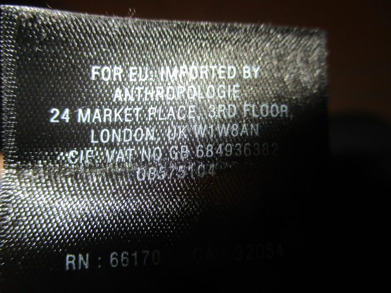 May include: Black and white label with the text "FOR EU: IMPORTED BY ANTHROPOLOGIE 24 MARKET PLACE 3RD FLOOR LONDON, UK WIW8AN CIF VAT NO GB-684936382 08575104 RN: 66170 CA 32054"