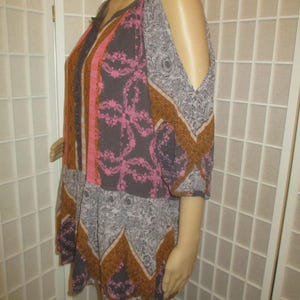 May include: A patterned, open-shoulder top in shades of gray, pink, and brown. The top features a V-neckline and a mix of floral and geometric designs. The sleeves are short and the fabric appears lightweight.