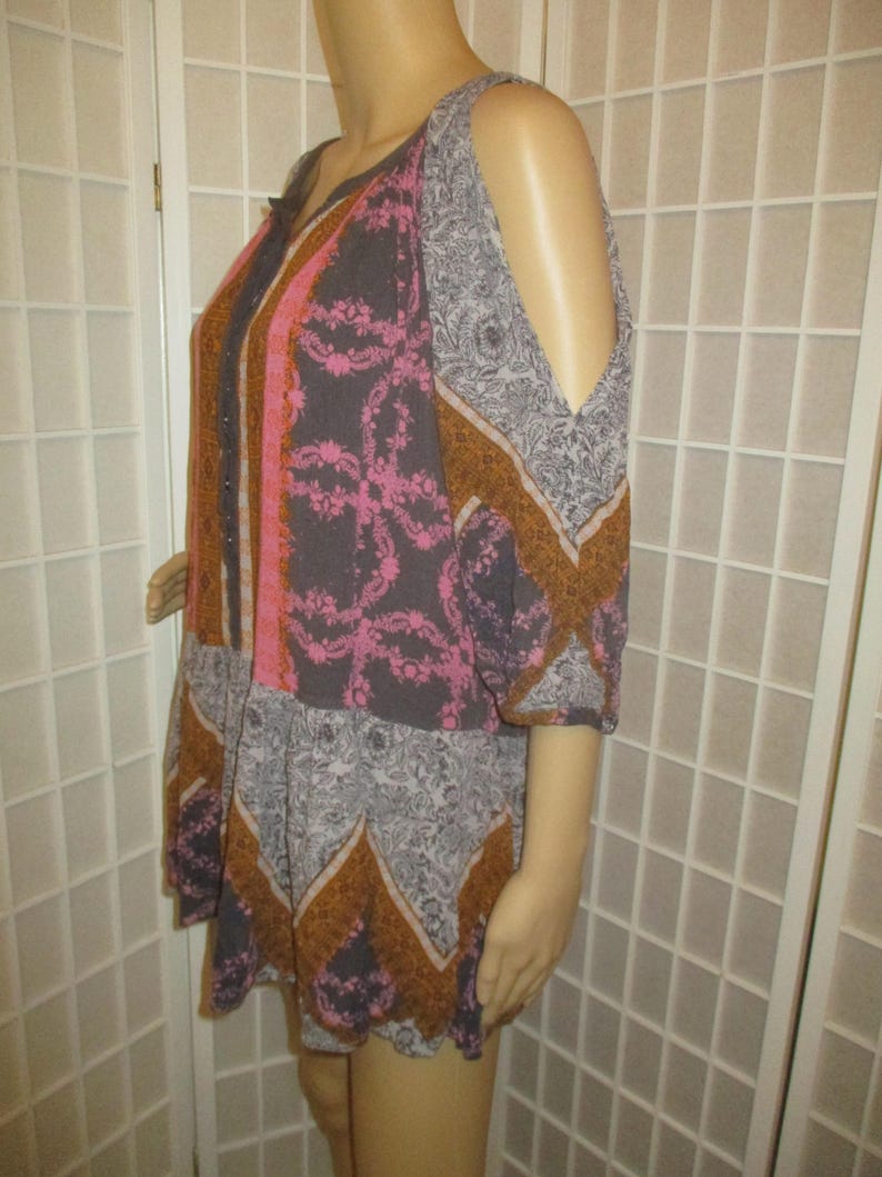 May include: A patterned, open-shoulder top in shades of gray, pink, and brown. The top features a V-neckline and a mix of floral and geometric designs. The sleeves are short and the fabric appears lightweight.