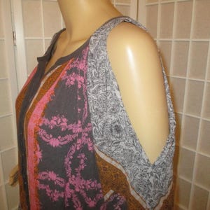 May include: A sleeveless top with a floral and paisley pattern in shades of gray, pink, and brown. The top has a round neckline and cut-out shoulder details. The fabric appears to be lightweight.