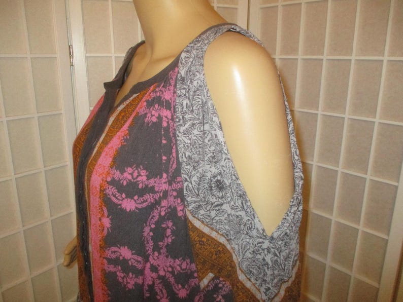 May include: A sleeveless top with a floral and paisley pattern in shades of gray, pink, and brown. The top has a round neckline and cut-out shoulder details. The fabric appears to be lightweight.