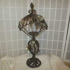 May include: A black metal candle holder with a decorative design of leaves and crystals. The holder has a tall, slender base and a wide, open top.