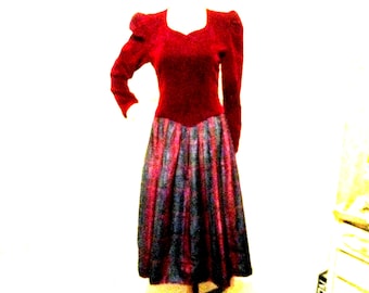 May include: A vintage red dress with long sleeves and a square neckline. The bodice is a solid red, while the skirt features vertical stripes in shades of red, blue, and black. The dress is displayed on a mannequin.