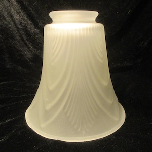 May include: A frosted glass lampshade with a flared, bell-like shape. The shade features a series of vertical, curved lines that create a textured pattern. The top of the shade has a slightly narrower opening, and the overall design is simple and elegant.