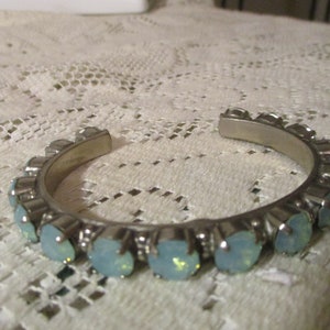 May include: A silver bangle bracelet with a row of light blue, iridescent stones.