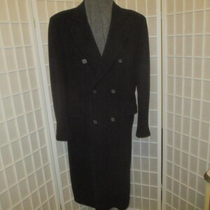 May include: A long, black, double-breasted overcoat featuring a notched lapel collar, long sleeves, and a structured silhouette. The coat is fastened with two columns of dark buttons down the front, creating a classic and formal appearance.