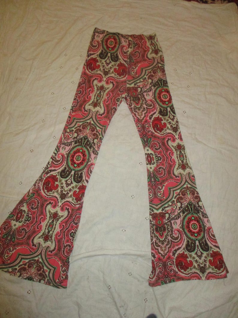 Puede incluir: Pantalones acampanados con un vibrante estampado de cachemira en tonos rojos, rosas, marrones y crema. Los pantalones est&aacute;n extendidos, mostrando toda la longitud y el intrincado dise&ntilde;o. La tela parece suave y ligera.