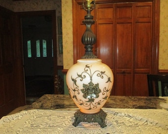 May include: A vintage table lamp with a white glass base featuring a floral design. The base is decorated with a large rose and intricate scrollwork. The lamp has a bronze-colored metal stem and finial.