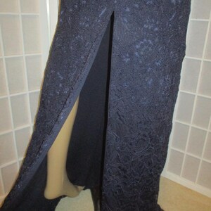 May include: A long, navy blue lace dress with a slit up the front. The dress is made of a delicate lace fabric and has a flowing silhouette.