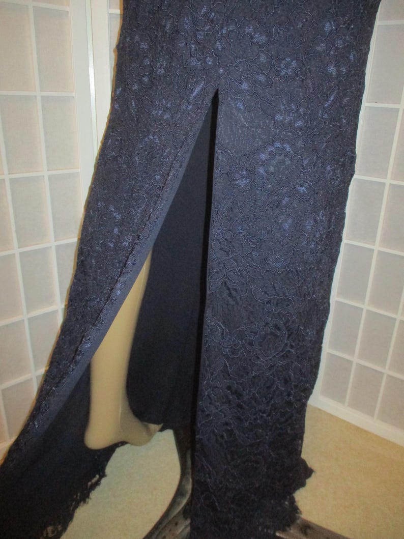 May include: A long, navy blue lace dress with a slit up the front. The dress is made of a delicate lace fabric and has a flowing silhouette.