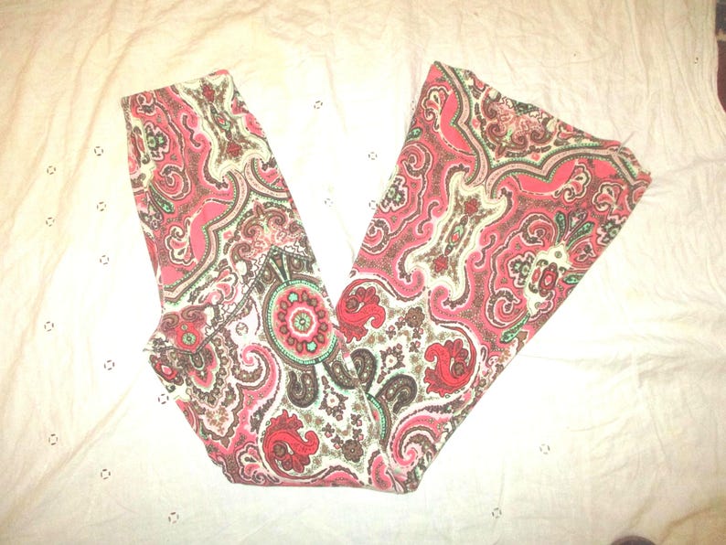 Puede incluir: Pantalones con estampado de cachemira en tonos rojos, rosas, marrones y blancos. La tela presenta un dise&ntilde;o detallado y arremolinado con elementos florales y abstractos. Los pantalones est&aacute;n doblados, mostrando el patr&oacute;n completo.