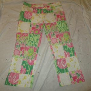 May include: A pair of pants featuring a patchwork design of alternating squares. The pattern includes white squares with yellow floral accents and green and pink squares decorated with illustrations of tulips, hearts, and various flowers.