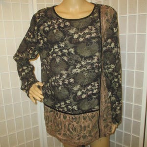 May include: A long-sleeved tunic with a floral pattern in shades of black, green, and cream. The tunic has a round neckline and a contrasting panel on the side and hem. The fabric appears to be lightweight and flowing.