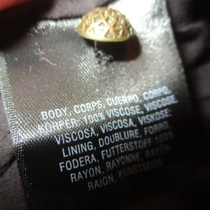 May include: A black fabric label with white text detailing the fabric composition of the garment. The text reads: "BODY, CORPS, CUERPO, CORPO KORPER: 100% VISCOSE, VISCOSE VISCOSA, VISCOSA, VISKOSE LINING, DOUBLURE, FORRO FODERA, FUTTERSTOFF 100% RAYON, RAYONNE, RAYON RAION, KUNSTSEIDE"