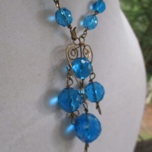 May include: A blue glass bead necklace with a gold wire pendant featuring a heart design and dangling blue glass beads.
