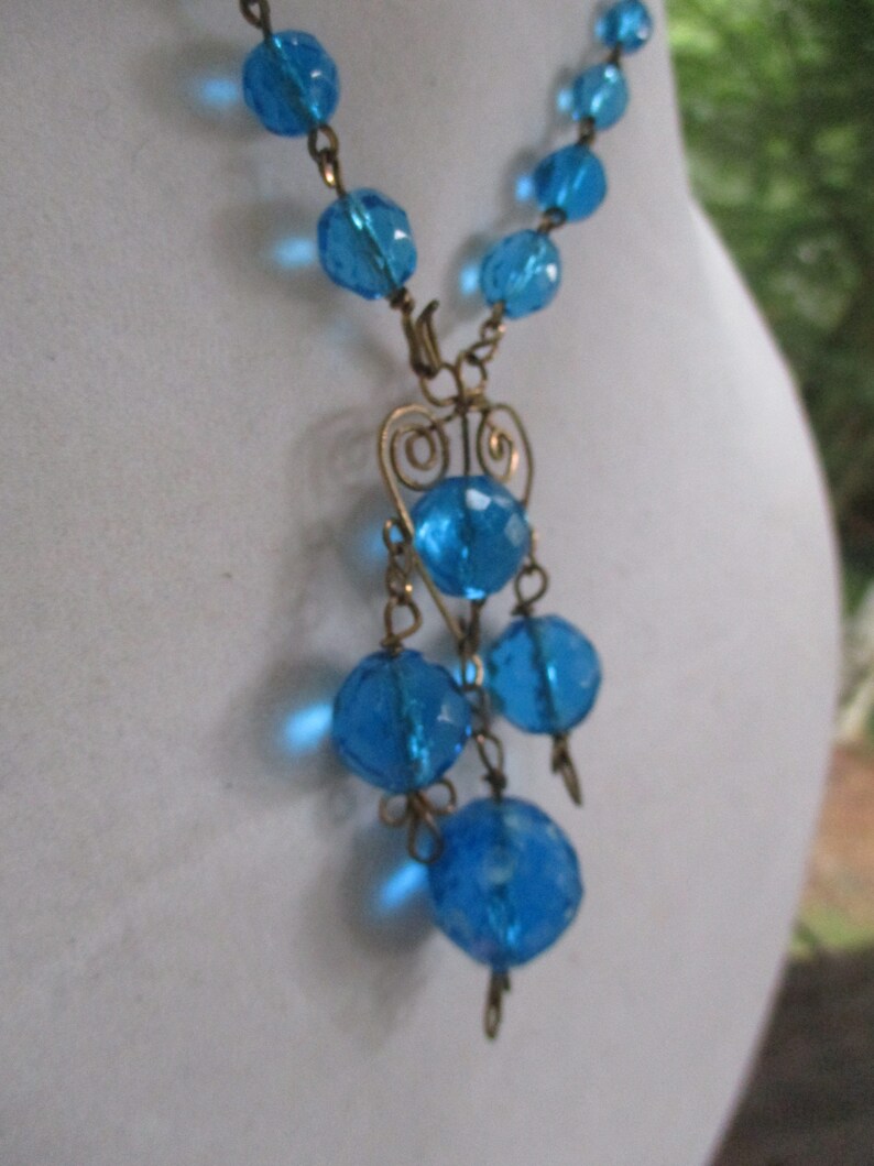 May include: A blue glass bead necklace with a gold wire pendant featuring a heart design and dangling blue glass beads.