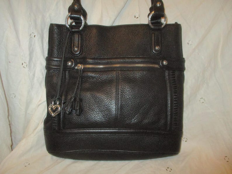 May include: Black leather tote bag with silver-tone hardware. Features a zipped top, front pocket, and decorative tassels. The bag has two top handles and a heart-shaped charm.