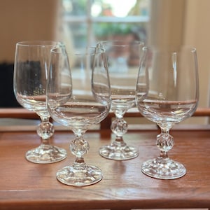 May include: A set of four clear glass goblets with smooth, rounded bowls and stems featuring a faceted, diamond-cut spherical accent above a circular base. The glassware is transparent and colorless, showcasing a reflective, geometric design.