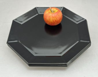 Può includere: Una pila di piatti neri ottagonali con finitura lucida. Una mela rossa e gialla è appoggiata sopra i piatti. I piatti hanno un design geometrico moderno, adatto per servire cibo.