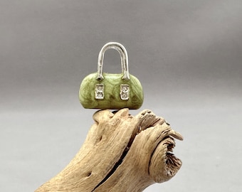 Può includere: Una piccola borsa a mano verde con manico argentato e strass. La borsa è appoggiata su un pezzo di legno galleggiante.