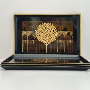 May include: Set of three black rectangular trays with a gold tree and forest design. The trays have a gold border and a glossy finish. The tree design is centered on the tray, with a forest of trees in the background.