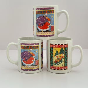 May include: Three white ceramic mugs with Christmas-themed designs. Two mugs feature Santa Claus with the word "BELIEVE". The third mug shows a child sledding with the words "MERRILY MERRILY".