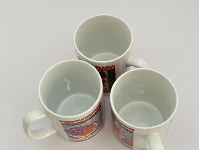 Puede incluir: Tres tazas de cer&aacute;mica blanca con asas, cada una con una banda decorativa colorida alrededor del centro. Las bandas muestran un dise&ntilde;o festivo con una combinaci&oacute;n de colores rojo y verde. Las tazas est&aacute;n vac&iacute;as y dispuestas sobre una superficie blanca.