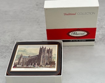 Puede incluir: Un juego de posavasos cuadrados en una caja blanca con la etiqueta Traditional Collection Pimpernel De Luxe Finish. El posavasos superior presenta una ilustración detallada de la Abadía de Westminster sobre un fondo de color crema.