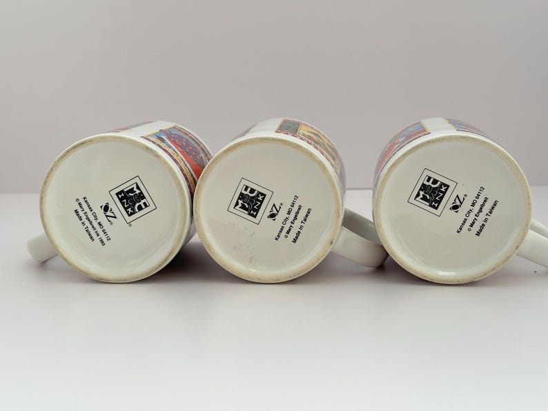 Puede incluir: Tres tazas de cer&aacute;mica blanca con asas, cada una con un dise&ntilde;o colorido alrededor del borde. La base de cada taza presenta un logotipo y el texto "Kansas City, MO 64112" y "Made in Taiwan."