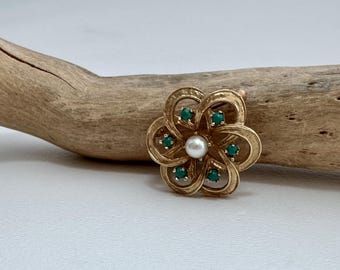Può includere: Un fermaglio dorato a forma di fiore con un centro di perla e pietre preziose verdi.
