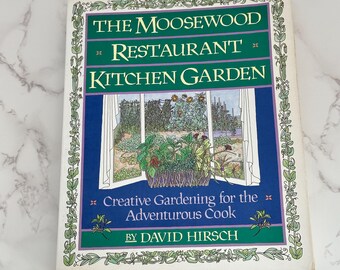 Può includere: Un libro intitolato "THE MOOSEWOOD RESTAURANT KITCHEN GARDEN" con una copertina verde e blu. La copertina presenta una scena di finestra con piante e il testo "Creative Gardening for the Adventurous Cook" di David Hirsch.