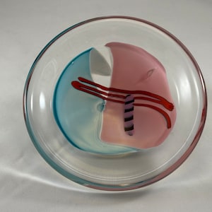 May include: A clear glass bowl with a pink, blue, and white design. The design features a swirl of colors and a thin black and white stripe.