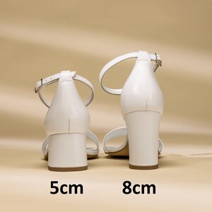 Puede incluir: Dos pares de sandalias de tac&oacute;n de cuero blanco con tiras de tobillo. Las sandalias de la izquierda tienen un tac&oacute;n de 5 cm y las sandalias de la derecha tienen un tac&oacute;n de 8 cm.