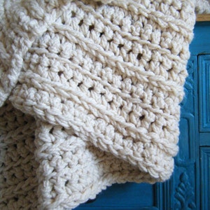Puede incluir: Una manta de crochet blanca con un patrón texturizado. La manta está drapeada sobre una cómoda pintada de azul.