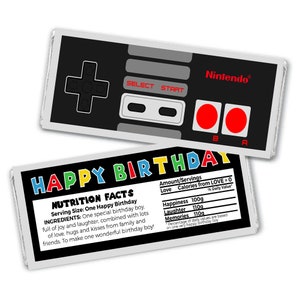 May include: A chocolate bar wrapper with a retro video game controller design. The wrapper is white with a black and gray controller design. The text "Nintendo" is printed in white on the top right corner of the wrapper. The text "HAPPY BIRTHDAY" is printed in rainbow colors on the bottom of the wrapper. The wrapper also includes a nutrition facts label with the text "NUTRITION FACTS" printed in black. The label lists the ingredients as "One special birthday boy, full of joy and laughter, combined with lots of love, hugs and kisses from family and friends. To make one wonderful birthday boy!" The label also lists the amount of happiness, laughter, and memories in grams.