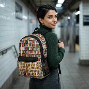 Può includere: Uno zaino con un colorato design a libreria. Lo zaino ha una tasca frontale e spallacci neri. Il corpo principale dello zaino è ricoperto da una stampa di libri sugli scaffali, con una varietà di colori.