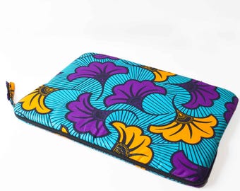 May include: A rectangular, padded laptop sleeve with a vibrant floral pattern. The design features large purple and yellow flowers on a turquoise background with black trim and a yellow zipper pull. The sleeve is designed to protect a laptop.