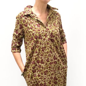 May include: A long-sleeved, collared dress with a floral print in shades of green, burgundy, and white. The dress has a v-neck and pockets on the sides.