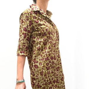May include: A long-sleeved shirt dress with a floral print in shades of green, brown, and white. The dress has a collared neckline and a button-up front.