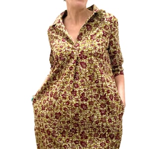 May include: A long-sleeved shirt dress with a collared neckline and button closure. The dress is made of a green and burgundy fabric with a floral pattern.