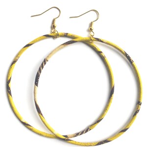 May include: A pair of large hoop earrings. The hoops are covered in a yellow fabric with a brown and tan pattern. The earring hooks are gold-colored.