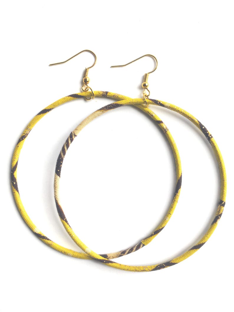 May include: A pair of large hoop earrings. The hoops are covered in a yellow fabric with a brown and tan pattern. The earring hooks are gold-colored.