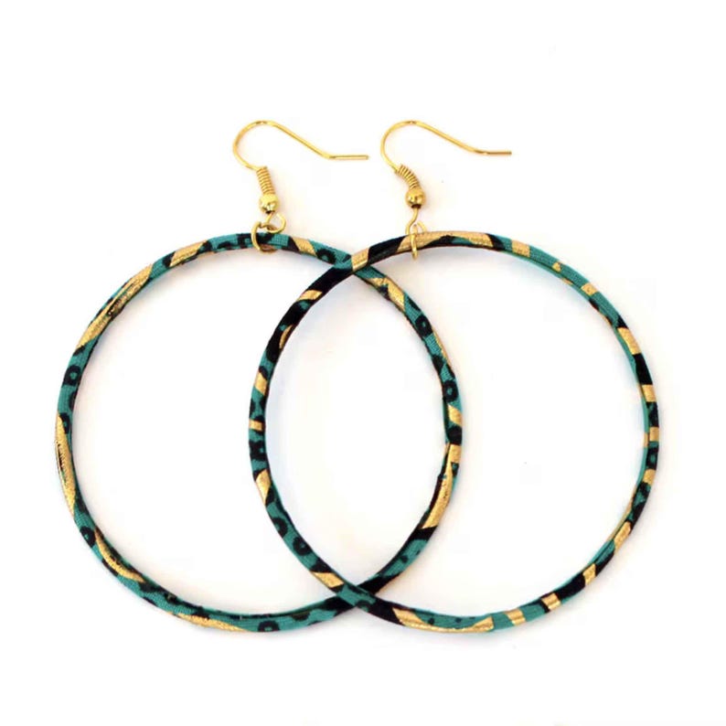 May include: A pair of large hoop earrings with gold-colored hooks. The hoops are decorated with a teal, black, and gold patterned fabric. The earrings are displayed against a white background.