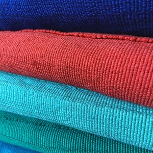 Puede incluir: Pila de cinco muestras de tela en diferentes tonos de azul, rojo y verde. La tela es un material tejido con una superficie texturizada.