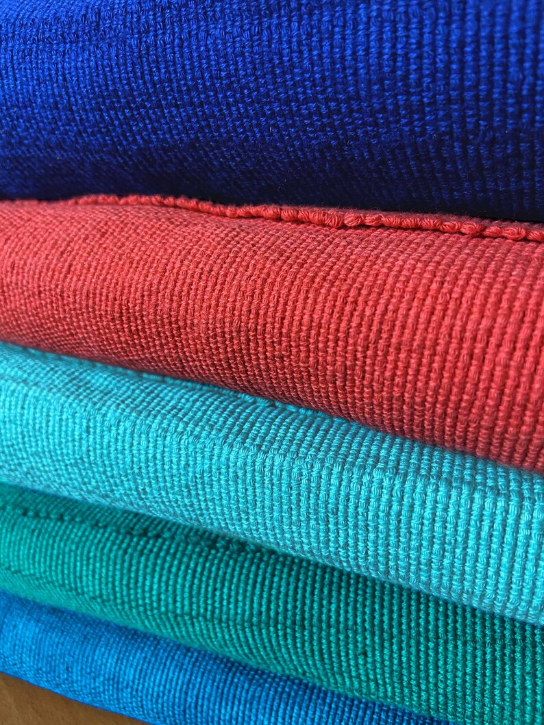Puede incluir: Pila de cinco muestras de tela en diferentes tonos de azul, rojo y verde. La tela es un material tejido con una superficie texturizada.
