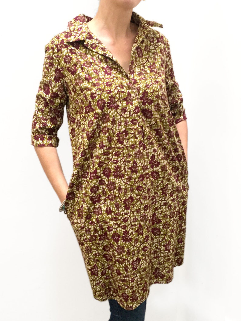 May include: A long-sleeved, collared dress with a floral print in shades of green, burgundy, and white. The dress has a v-neck and pockets on the sides.